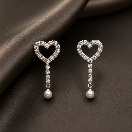 Heart-shaped earrings with pearl drops on a dark fabric background