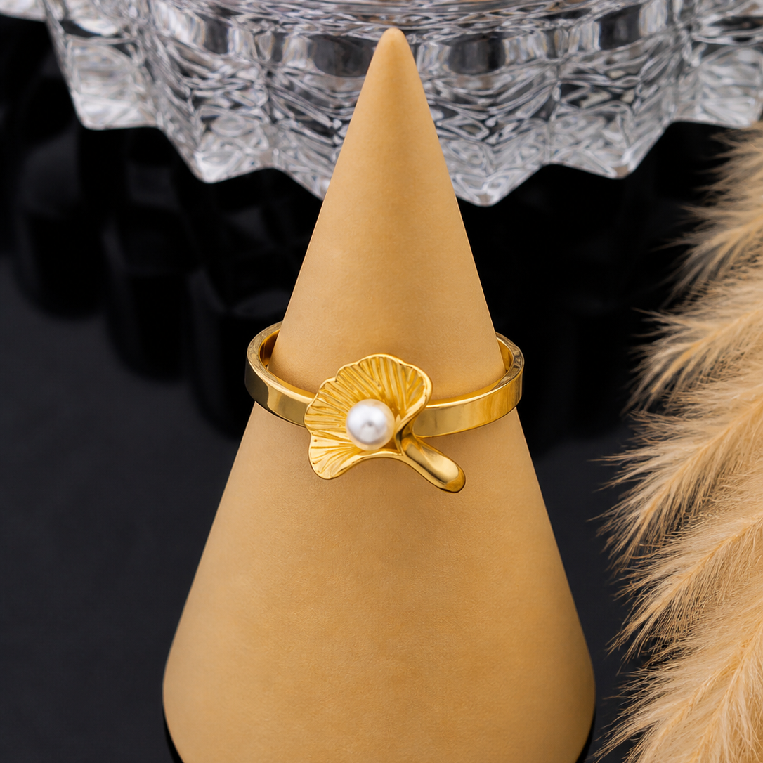 Gold ring with a pearl on a beige cone-shaped stand against a decorative background.