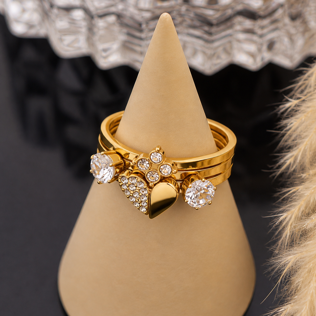 Gold ring with heart design and clear stones on a beige stand.