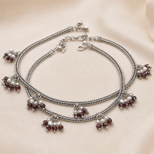 Stack of silver bracelets with pearl and garnet charm on a beige fabric background

